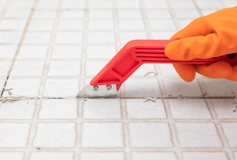Man using a grout rake to remove old grout from between bathroom tiles